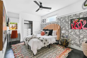 Un dormitorio con cama, escritorio, silla, ventilador de techo y pared con diseño de hojas.