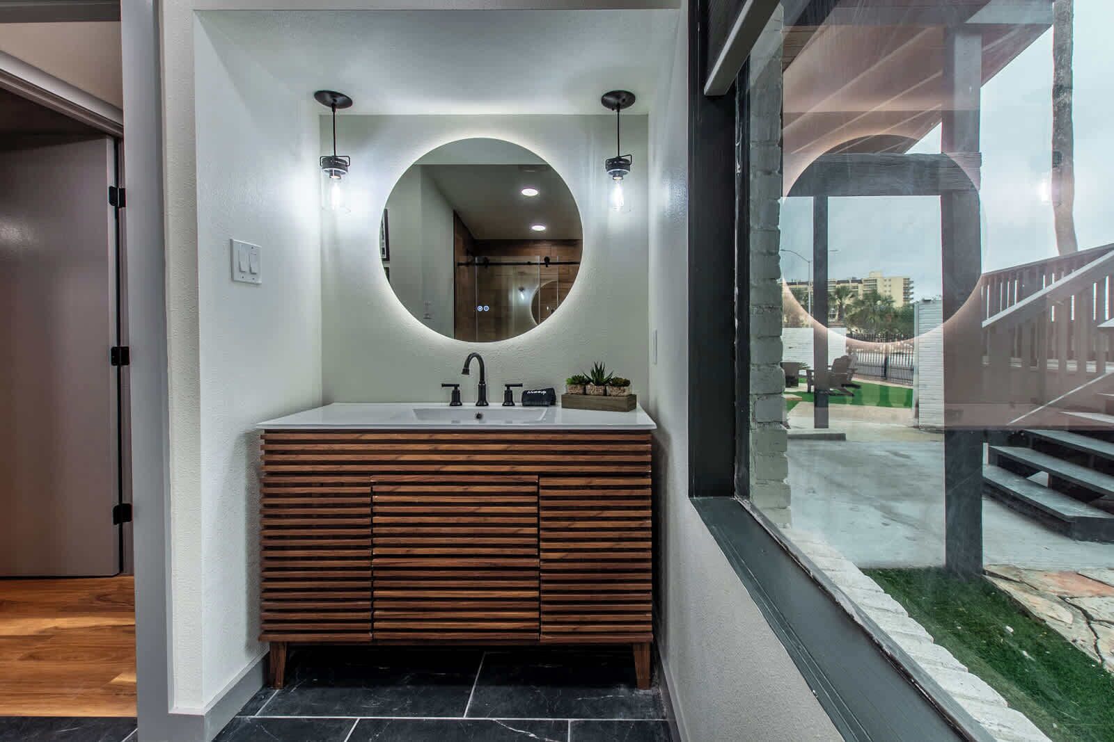 A modern bathroom with a wooden vanity, a large mirror, and a view of a staircase and outdoor area.