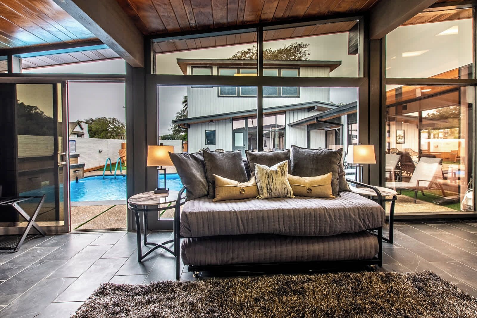 A modern bedroom with a large bed, a view of the backyard, and a glass door leading outside.