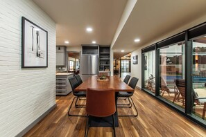 A modern kitchen with a large island, a dining area with a long table, and a view of the outdoors through large windows. - Luxury on Ocean Drive - Sleeps 28 (Corpus Christi)