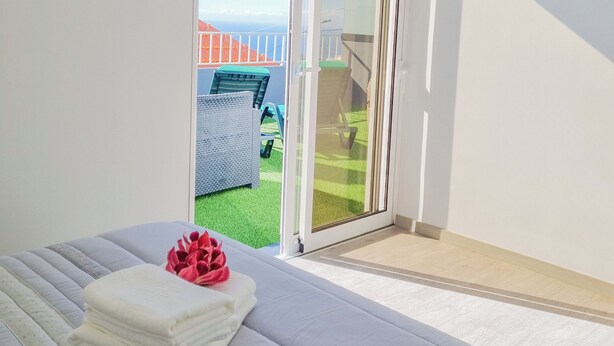 Une chambre à coucher avec un lit, une fenêtre donnant sur un jardin et une porte coulissante qui mène à un espace extérieur.