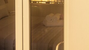 Une pièce avec un lit, une fenêtre donnant sur une balustrade et le reflet d’une source de lumière.