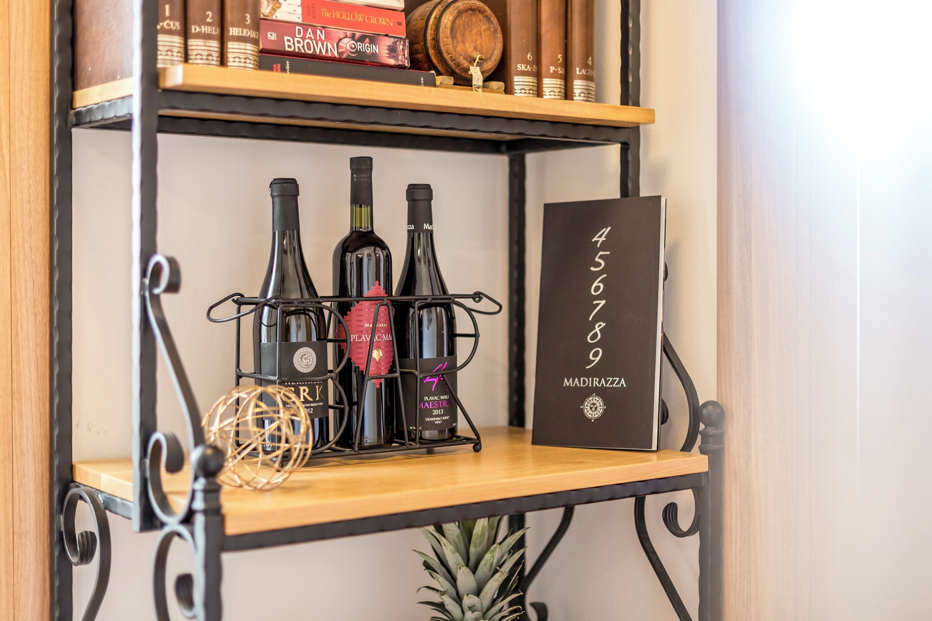 Una estantería de madera con botellas de vino y un botellero, una piña decorativa y un cartel con el número 456789.