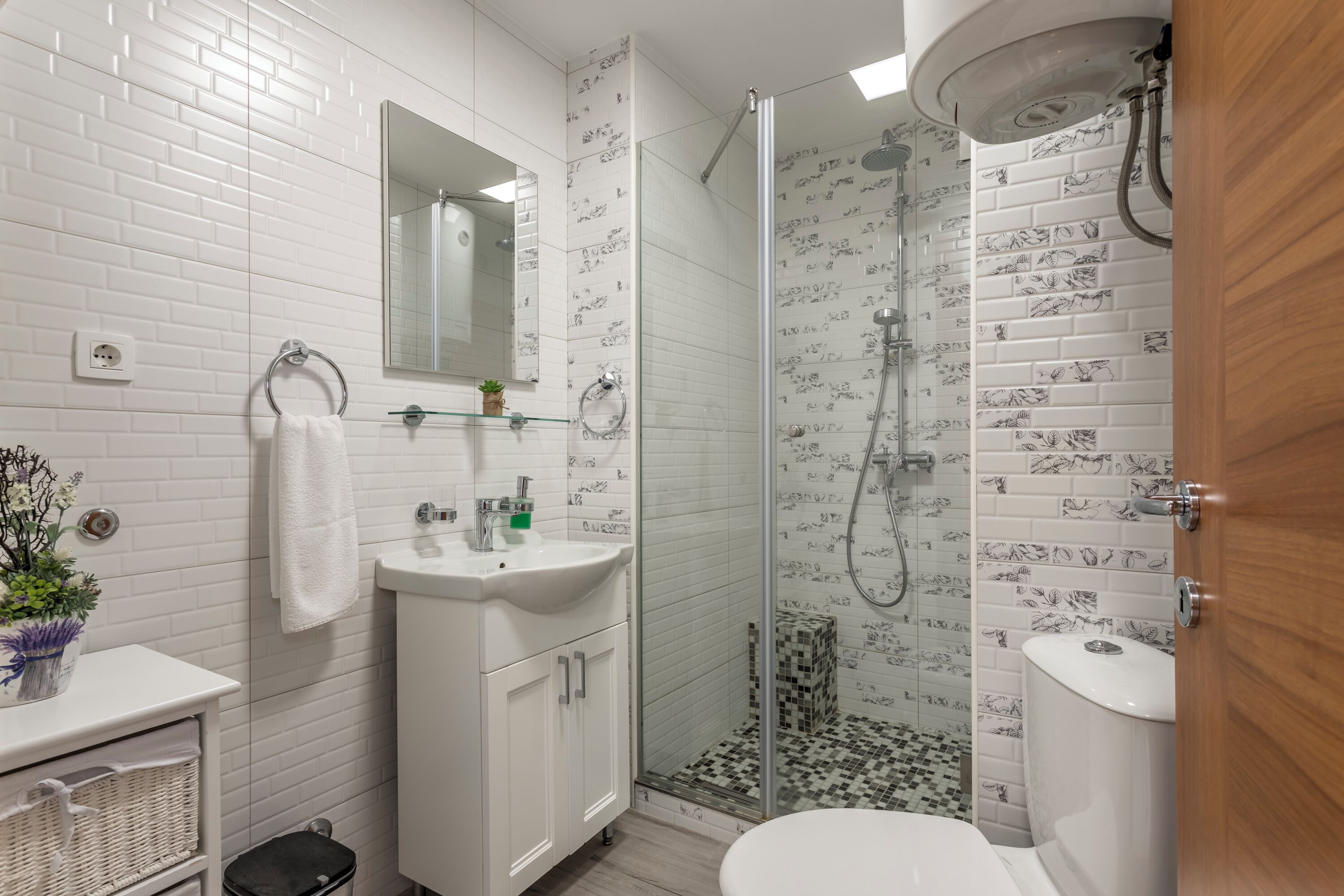 Een moderne badkamer met witte metrotegels, een glazen douchecabine, een witte wastafel en een toilet.