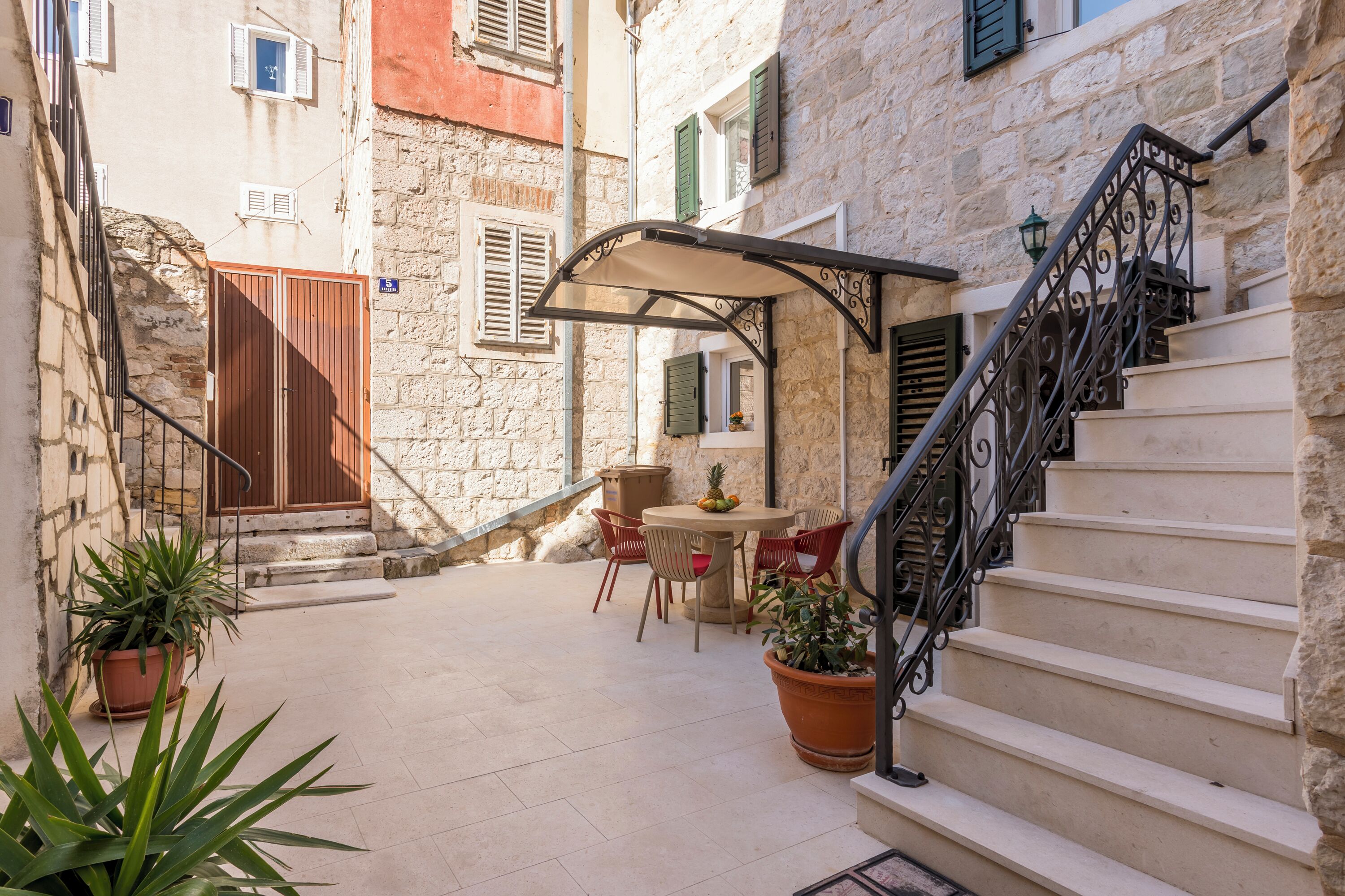 A courtyard with a table and chairs, a staircase, and potted plants.