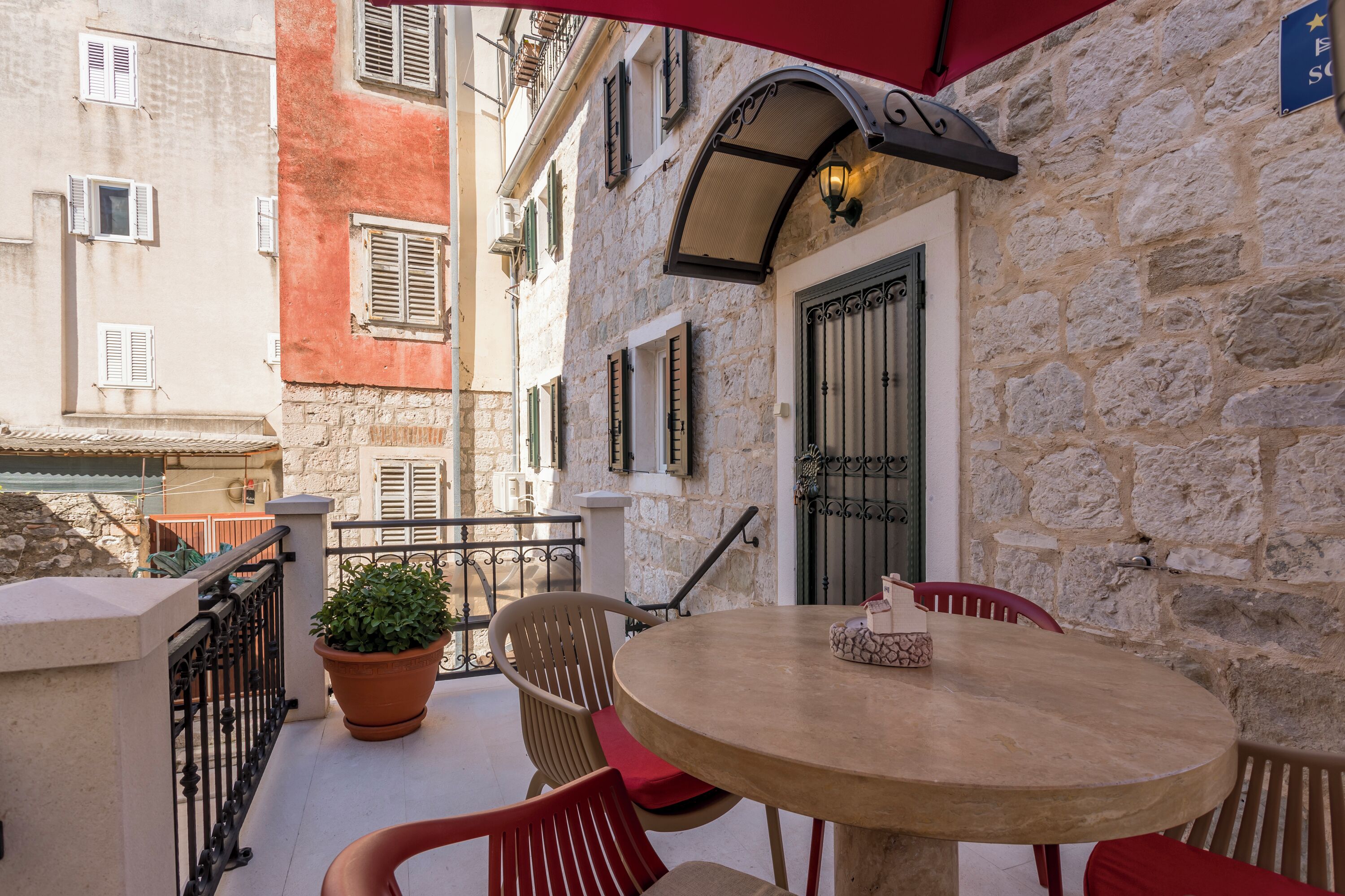 A stone building with a round table and red chairs on a balcony.