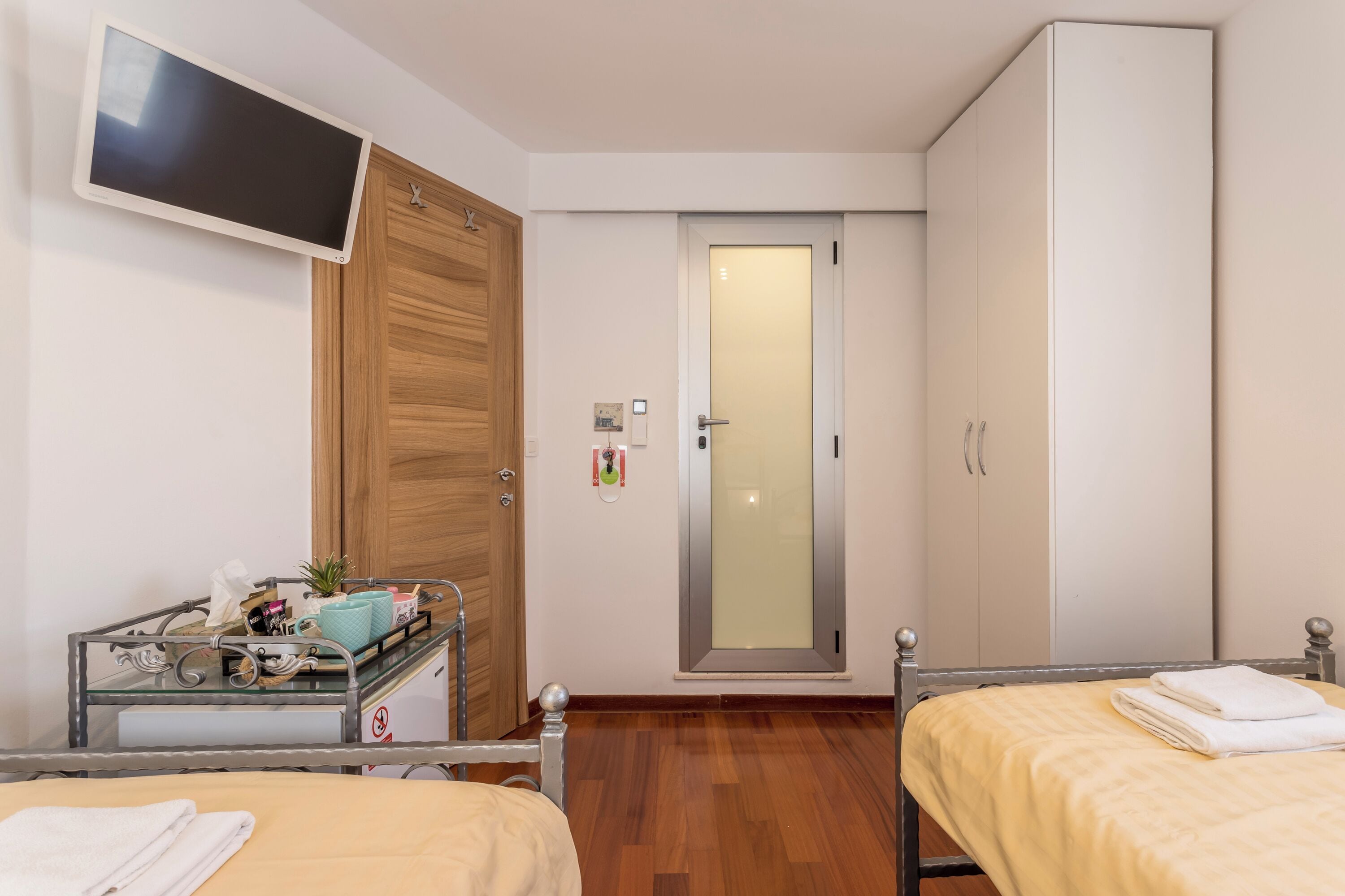 Habitació d'hotel amb dos llits, un televisor fixat a la paret, un armari i una taula petita amb articles de tocador.