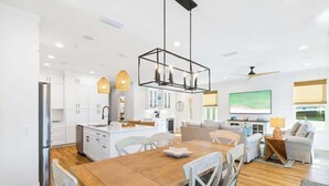 A modern kitchen with white cabinets, a wooden dining table, and a pendant light.