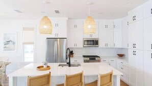 A modern kitchen with white cabinetry, a central island with chairs, a refrigerator, a stove, and pendant lights.
