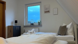 A bedroom with a large bed, a window with a view, a radiator, and a cabinet. - Vacation home Friesenkoje, in Loquard near Greetsiel and Emden, dogs allowed (Krummhörn)
