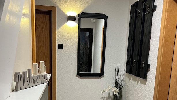 A hallway with a welcome sign, a mirror, a vase with flowers, and a dark rug on the floor. - Vacation home Friesenkoje, in Loquard near Greetsiel and Emden, dogs allowed (Krummhörn)