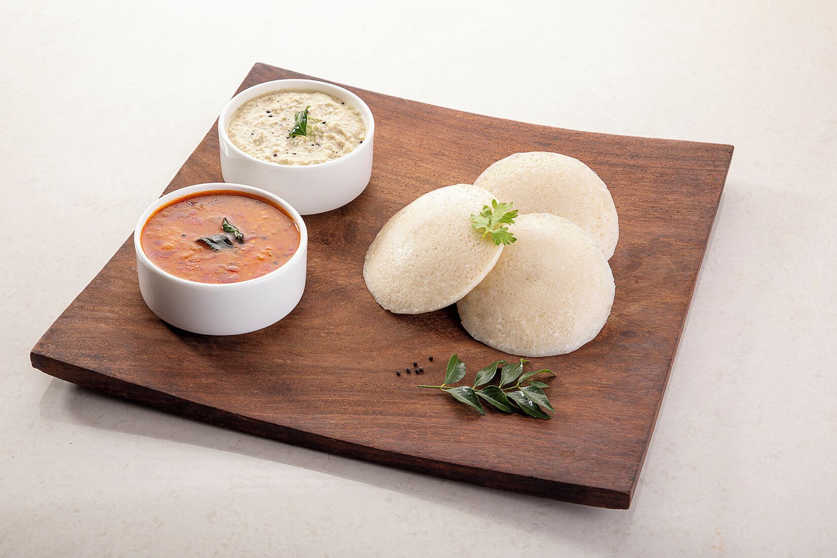 Een houten plank met drie idli's en twee chutneys.