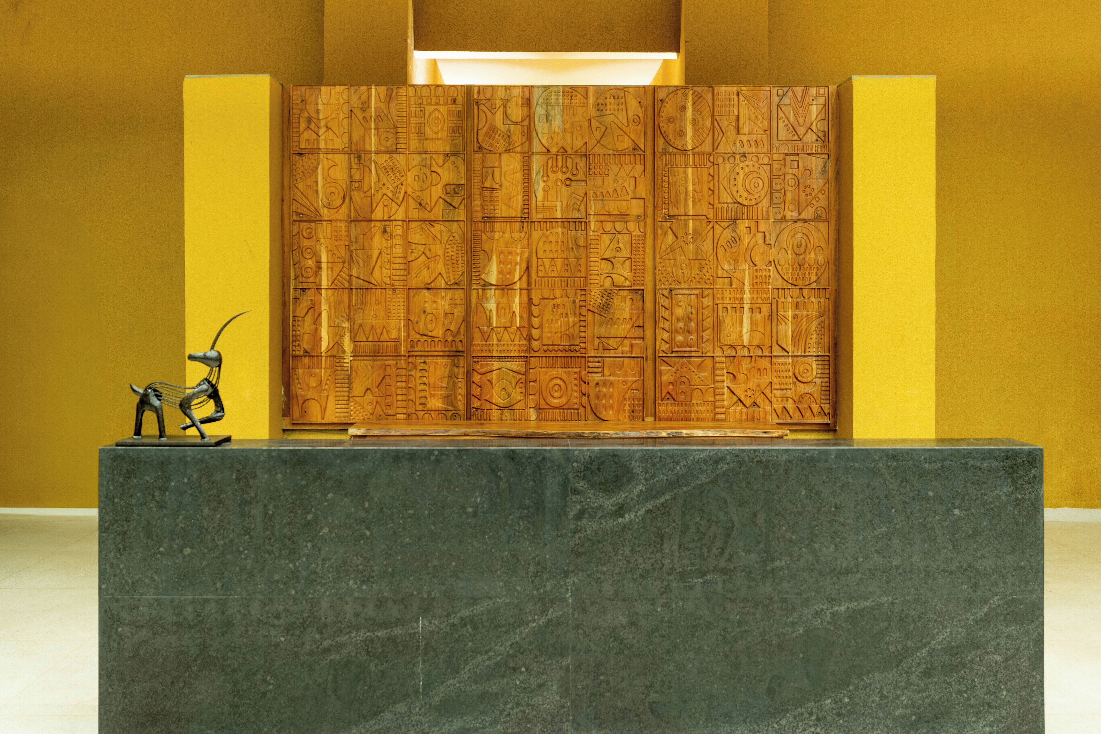 A reception desk with a carved wooden panel and a metal sculpture.