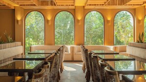 Een restaurant met een lange tafel en stoelen, grote gewelfde ramen en houten plafondpanelen.