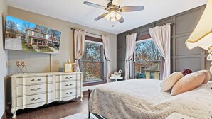 Un dormitorio con cama, cómoda, ventilador de techo y ventana con cortinas.