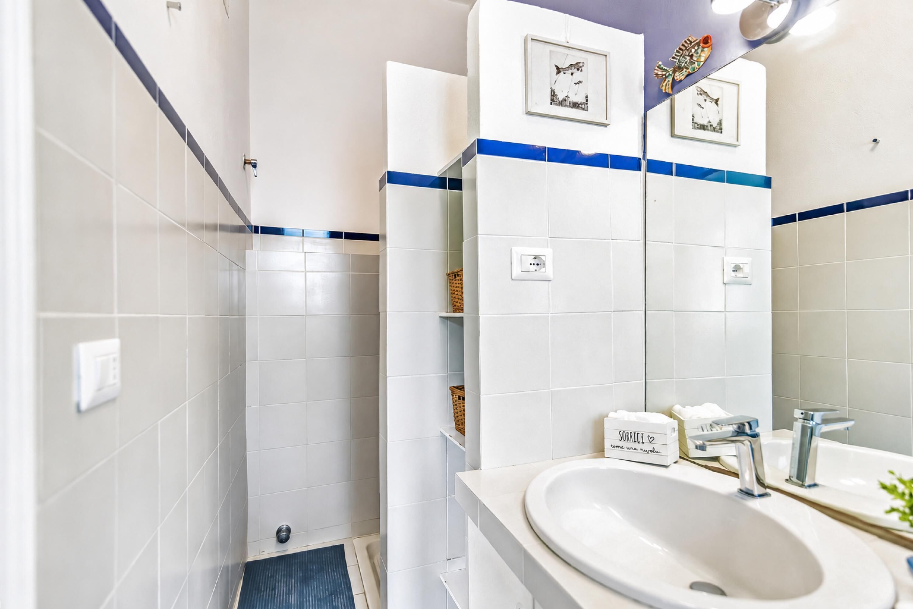 Un baño con azulejos blancos, un lavabo, un espejo y una zona de ducha.