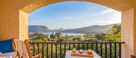 A balcony with a table set for breakfast, overlooking a scenic landscape with mountains and a lake.
