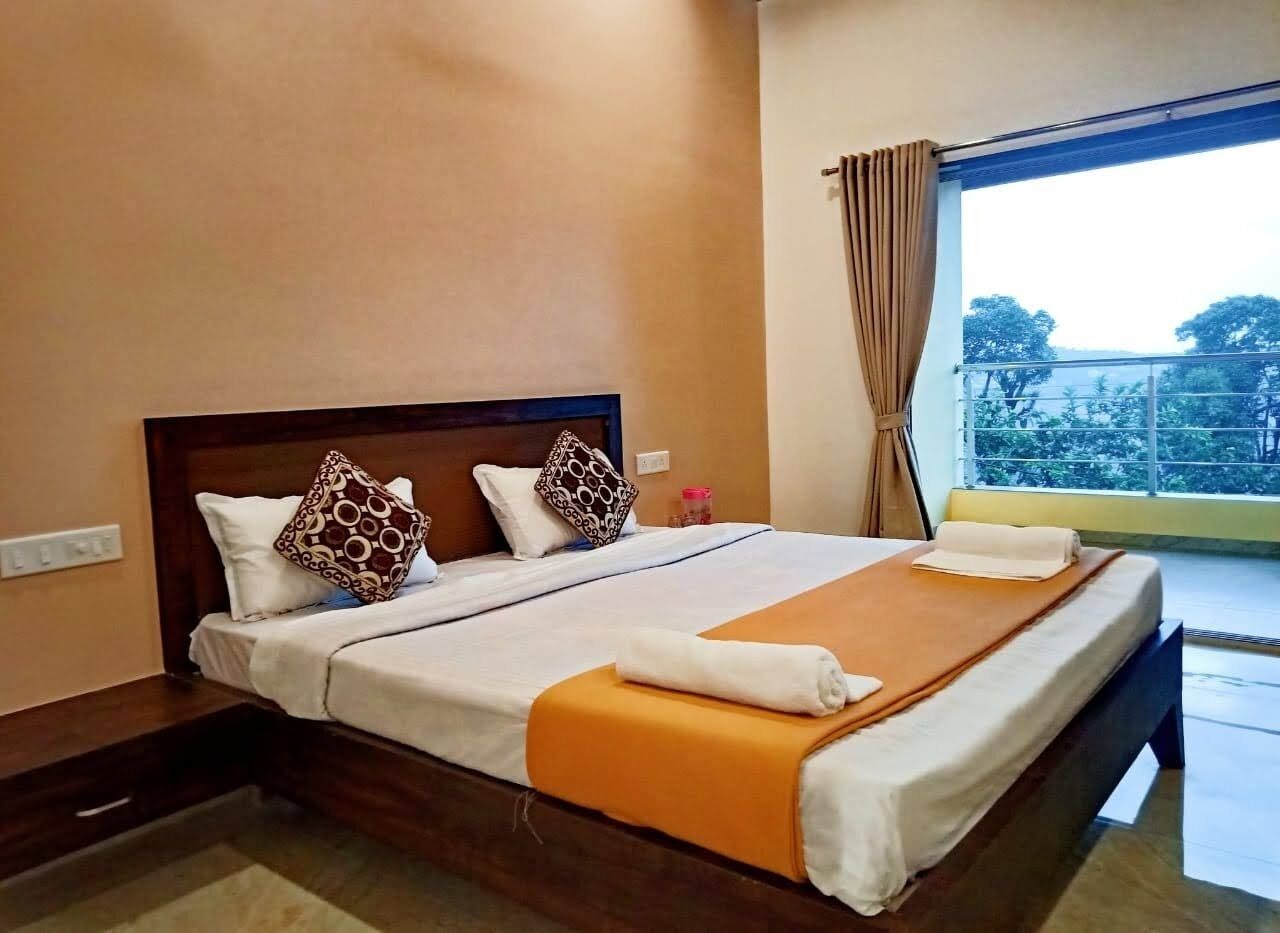 Una habitación de hotel con una cama grande, dos almohadas, una colcha y una ventana con cortinas.