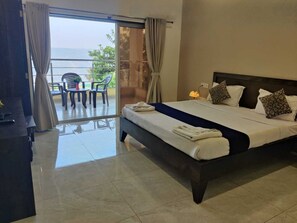 A hotel room with a large bed, a balcony with chairs, and a view of the sea. - Heaven Hills Resort (Mahabaleshwar)