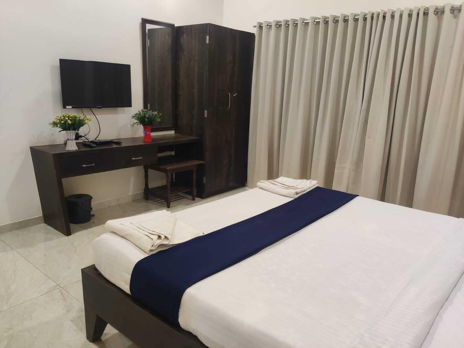 Une chambre d’hôtel équipée d’un lit, d’un bureau, d’une chaise, d’une armoire, d’une télévision et d’un rideau.