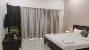 A hotel room with a bed, a bedside table with a lamp, and a curtain. - Heaven Hills Resort (Mahabaleshwar)