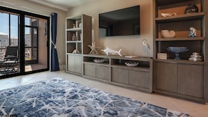 A modern living room with a large TV, built-in shelves with decorative items, a patterned rug, and a view through a glass door.