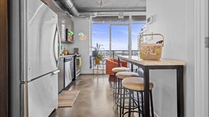 Een moderne keuken met roestvrijstalen apparatuur, een bar met krukken, en een groot raam met uitzicht op de stad.