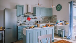 Une cuisine avec des armoires de couleur turquoise, un réfrigérateur en acier inoxydable, une table à manger en bois et un luminaire suspendu.
