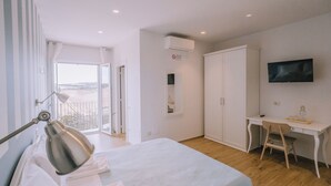 Une chambre avec un lit, un bureau, une chaise, une télévision et un balcon avec vue.