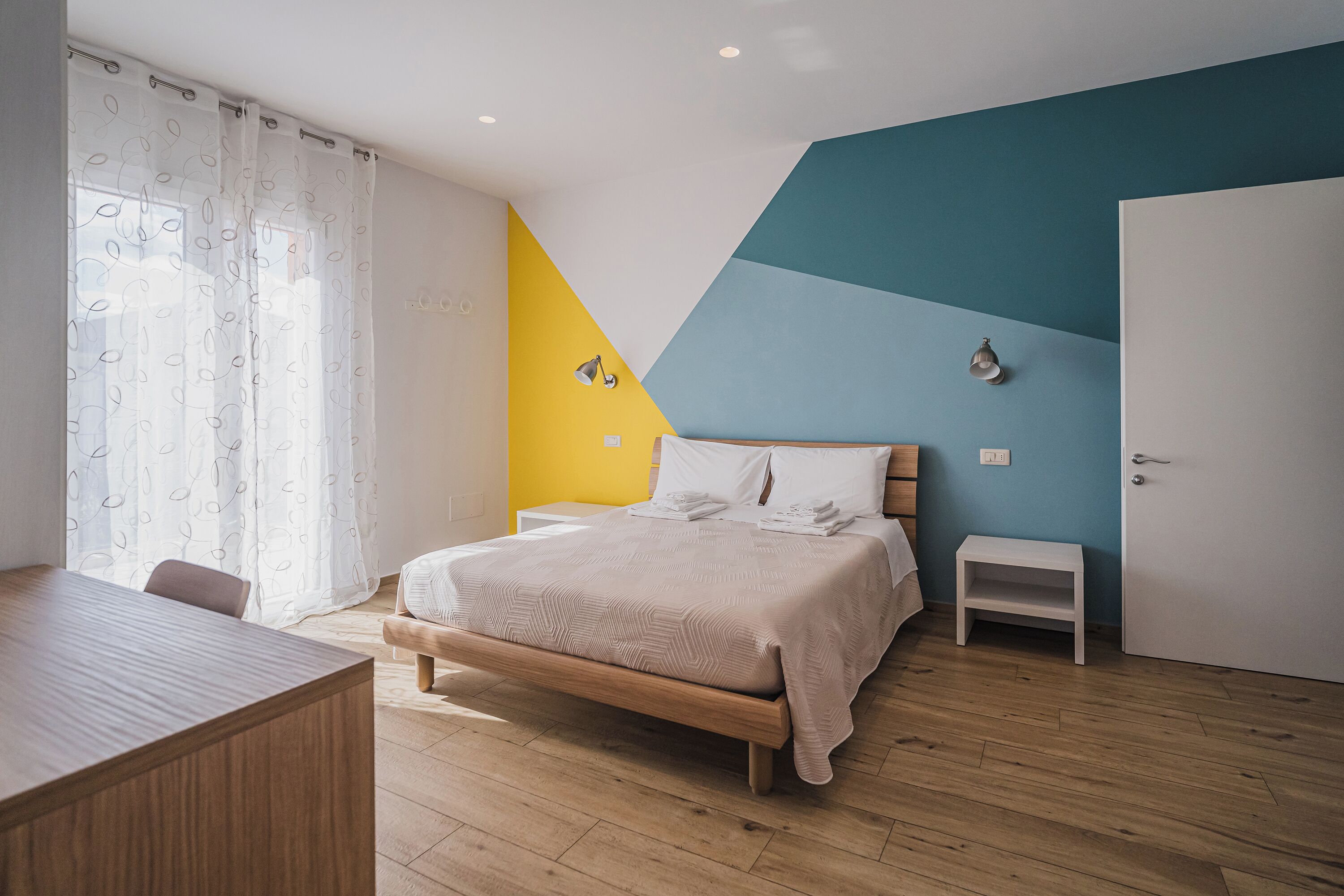 A bedroom with a bed, bedside tables, a desk, and a chair.