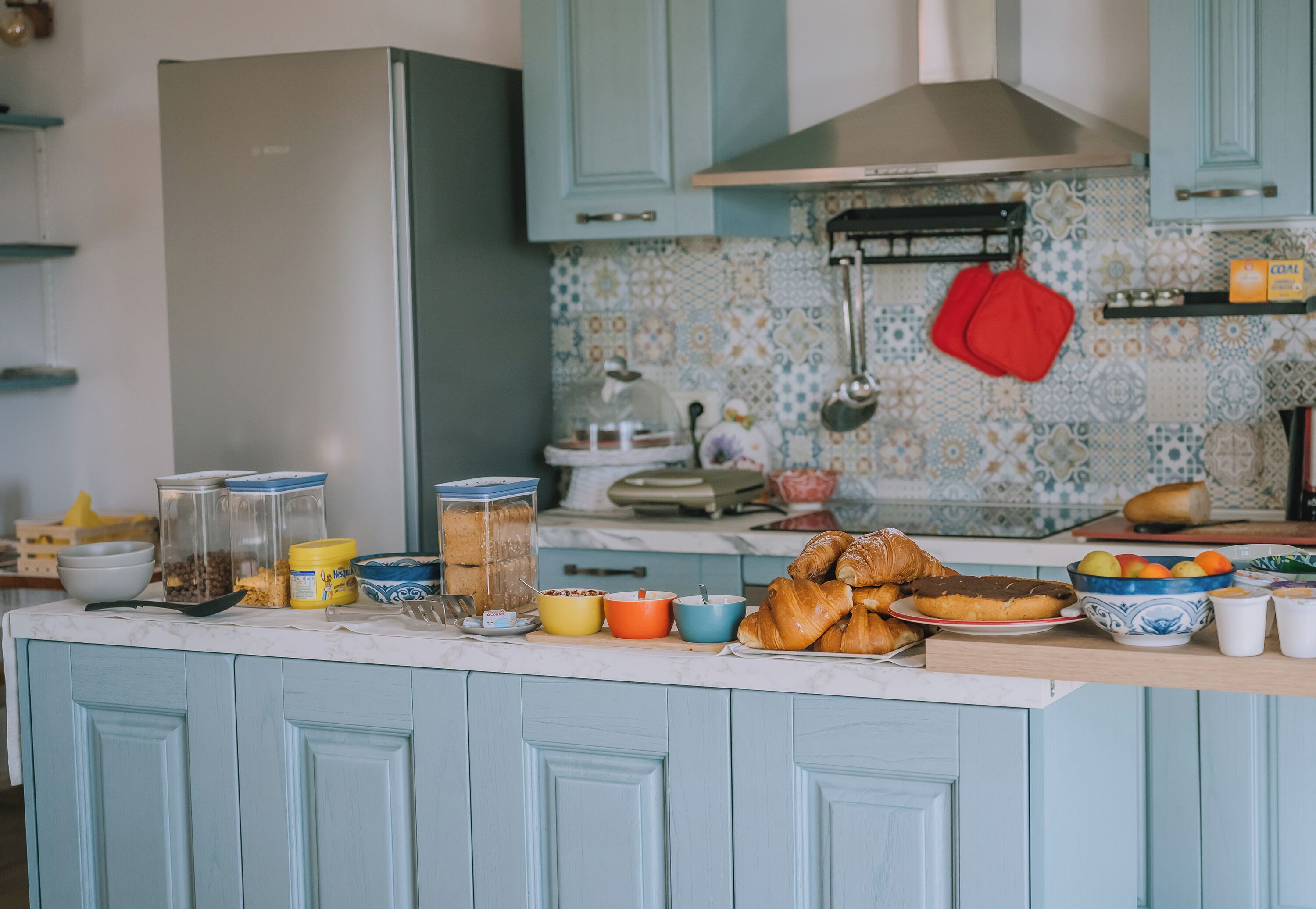 A kitchen with light blue cabinets, a tiled backsplash, and various food items on the counter.