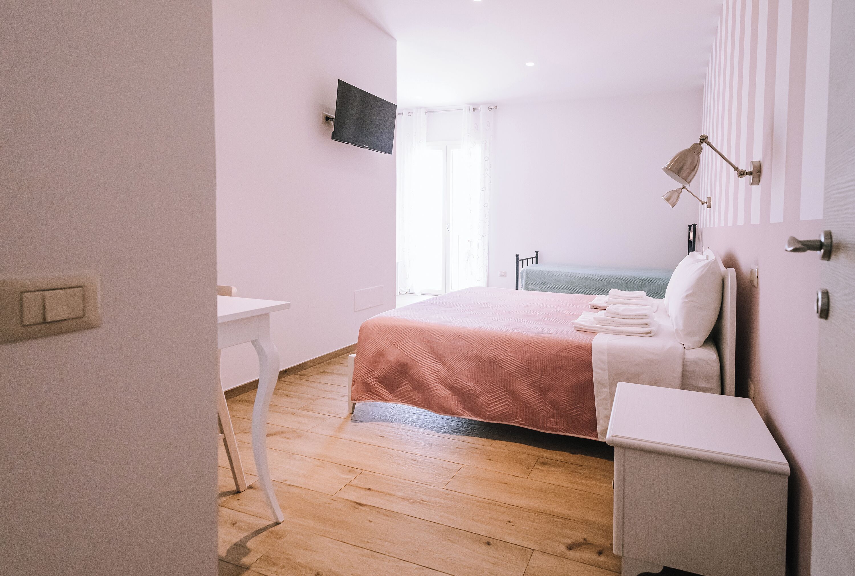 Quarto com cama, mesa de cabeceira e televisão na parede.