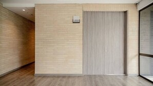 Un couloir avec un plancher en bois, un mur en briques et une porte fermée, au-dessus de laquelle est accrochée une enseigne.
