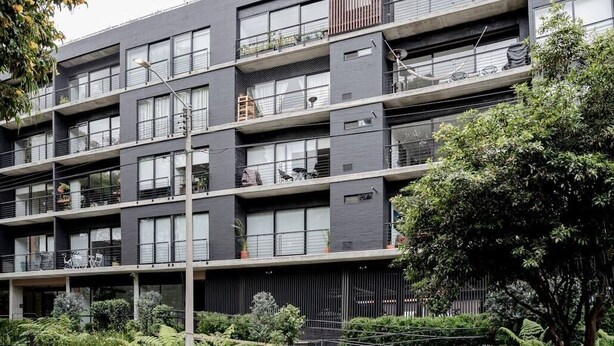 Un immeuble résidentiel à plusieurs étages, doté de balcons, d’un espace jardin et d’une architecture moderne.