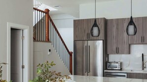Une cuisine moderne dotée d’appareils électroménagers en acier inoxydable, d’un escalier en bois et de luminaires suspendus.