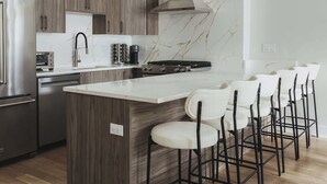 Une cuisine moderne dotée d’un îlot en marbre, d’appareils électroménagers en acier inoxydable et de luminaires suspendus noirs.