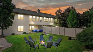 A two-story house with a backyard patio area featuring outdoor furniture and a fire pit. - Hot Tub - King Suite - Game Room - Large Groups (Sun Prairie)