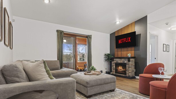 A modern living room with a fireplace, a flat-screen TV displaying 'NETFLIX', and a cozy seating arrangement. - Hot Tub - King Suite - Game Room - Large Groups (Sun Prairie)