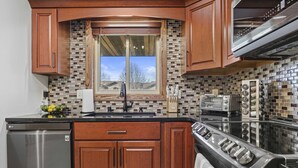 A kitchen with wooden cabinets, a stainless steel dishwasher, a black stove, and a window with a view of the outdoors. - Hot Tub - King Suite - Game Room - Large Groups (Sun Prairie)