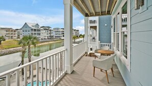 A wooden deck with a pool, overlooking a body of water and a row of buildings. - Experience luxury at Salt and Light in Ocean Isle Beach, perfect for 24 guests! (Ocean Isle)