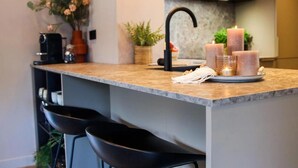 A modern kitchen with a marble countertop, black chairs, a coffee machine, and candles. - Dune Lagoon (Egmond aan den Hoef)