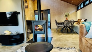 A modern living room with a fireplace, a television, and a dining area with chairs and a table. - Dune Lagoon (Egmond aan den Hoef)