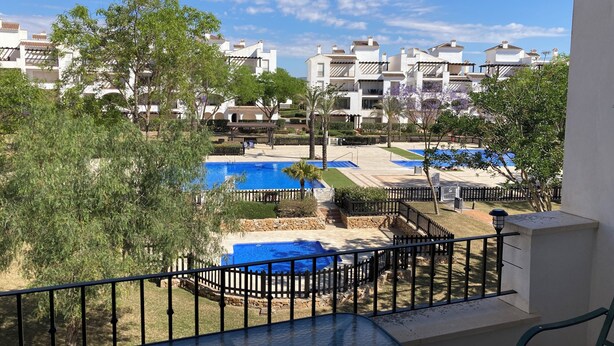 A view of a residential area with multiple white buildings, a swimming pool, and a fenced garden area.