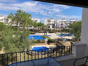 A view of a residential area with multiple white buildings, a swimming pool, and a fenced garden area. - Arty Apartment La Tore Golf Resort- central, pool view, close to amenities  (Torre-Pacheco)