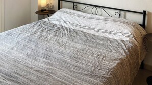 A neatly made bed with a patterned bedspread, a bedside lamp, and two abstract wall art pieces.