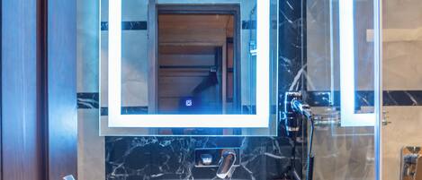 A bathroom with a marble backsplash, a large mirror, a sink, and a glass shower enclosure.