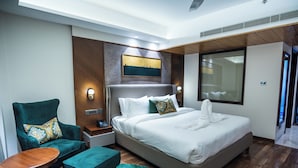 Ein modernes Hotelzimmer mit einem großen Bett, einem grünen Sessel, einem kleinen Holztisch und einem grünen Teppich.