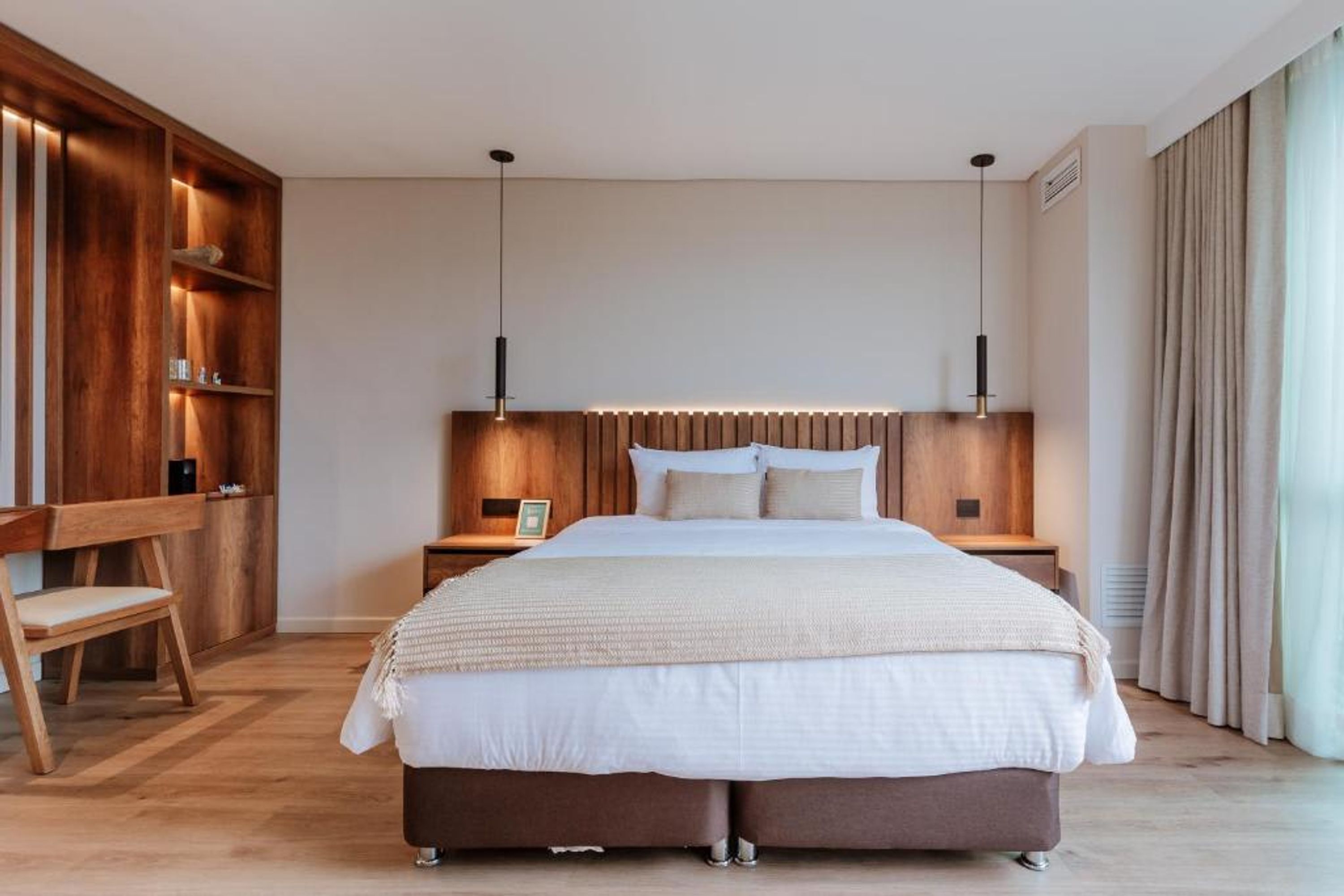 A modern bedroom with a large bed, wooden headboard, bedside tables, and a built-in wooden shelving unit.