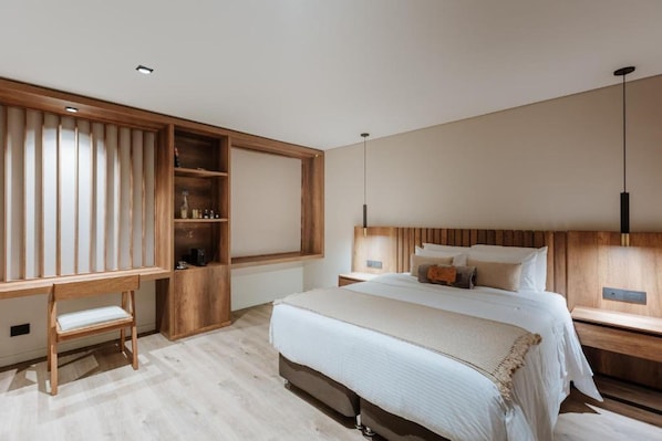 A modern bedroom with a large bed, wooden headboard, bedside tables, a desk, and a built-in shelving unit.