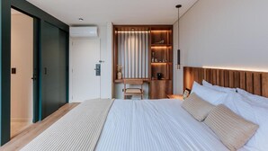 A modern hotel room with a large bed, a wooden headboard, a built-in desk with a chair, and a wall-mounted shelf with decorative items. - w Loft Estandar (Medellín)